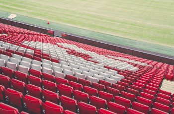 Rzędy czerwonych i białych krzesełek na trybunach stadionu piłkarskiego