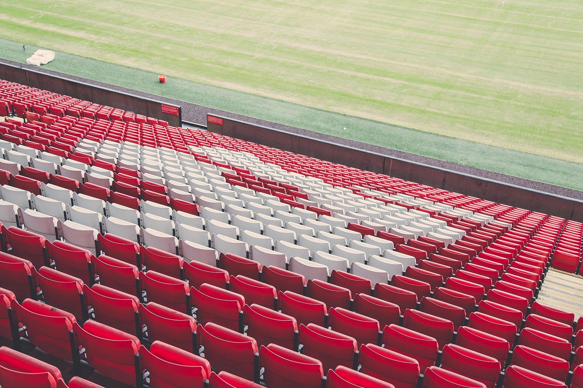 Rzędy czerwonych i białych krzesełek na trybunach stadionu piłkarskiego