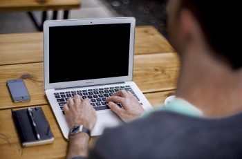 Mężczyzna wypełnia formularz na laptopie, obok telefon i notes z piórem