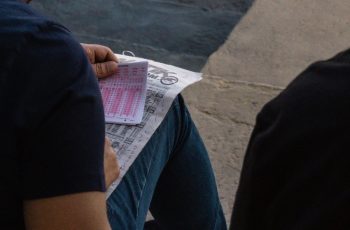 Osoba wypełnia kupon bukmacherski piórem, obok gazeta z notowaniami